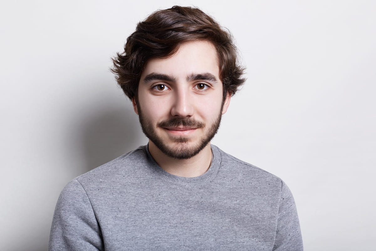 People and leisure concept. A portrait of handsome guy with beard and moustache with stylish hairstyle dressed in grey sweater isolated over white background having happy expression